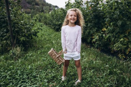 Téléchargez les photos : Petite fille aux cheveux blonds et aux yeux bleus joue joyeusement dans le jardin, apprécie la nature et l'air pur. Santé et joie des enfants. Bonne enfance - en image libre de droit