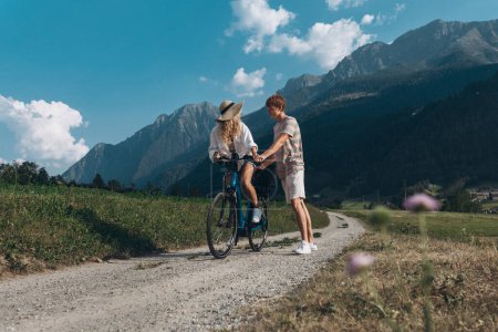 Foto de Dos amigos o pareja están en bicicleta a lo largo de la carretera. Deporte y vida activa sunset time concept. Pareja aprendiendo a andar en bicicleta, divirtiéndose juntos, viajando por las montañas cerca de la ciudad - Imagen libre de derechos