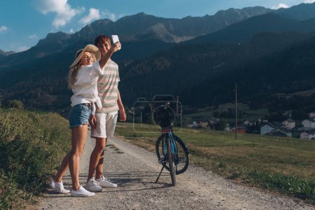 Foto de Dos amigos o pareja están en bicicleta a lo largo de la carretera. Deporte y vida activa sunset time concept. Pareja aprendiendo a andar en bicicleta, divirtiéndose juntos, viajando por las montañas cerca de la ciudad - Imagen libre de derechos