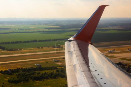 Téléchargez les photos : Une aile d'avion avec un bout d'aile pendant un vol au-dessus des champs - en image libre de droit