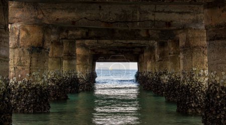 Perspective of the blue water from the coast beneath the concrete pier. View of the turquoise sea at the coast from beneath the concrete pier.