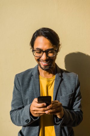 Téléchargez les photos : Une image verticale d'un homme d'affaires latino heureux regardant son téléphone portable avec le soleil du matin qui brille en arrière-plan - en image libre de droit