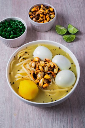 Foto de Plato tradicional peruano de sopa de pollo con tres huevos, fideos, tres huevos, cancha serrana y sus acompañamientos de limón, cebolla china. - Imagen libre de derechos