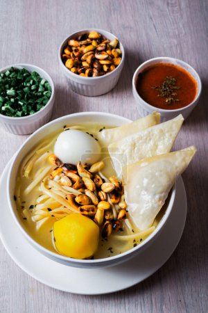 Foto de Plato de sopa de pollo con wuantan frito, fideos, huevo, patata amarilla, cancha serrana. Acompañado de cebolla china y rocoto. - Imagen libre de derechos