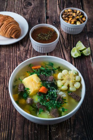 Foto de Sopa de sancocho con maíz, carne, zanahorias, calabaza, yuca. Acompañado de pan, cancha serrana, rocoto y limón. - Imagen libre de derechos