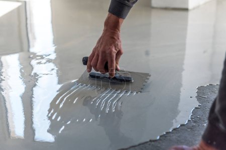 Photo for Construction workers are painting the floor using the method self-leveling epoxy.spreading self leveling compound with trowel.Self-leveling epoxy. Leveling with a mixture of cement floors. - Royalty Free Image