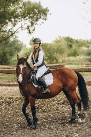 Foto de A young female jockey is sitting on her horse in show jumping training. Preparing for the competition. Love for horses. - Imagen libre de derechos