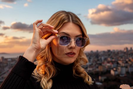 Hermosa modelo femenina con gafas de colores al atardecer. Retrato romántico al aire libre de una atractiva mujer rubia con maquillaje y gafas posando. Archipiélago de Estambul (Islas Princesas) skyline.