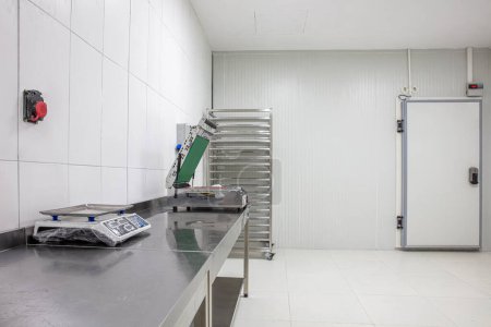 Cold room in warehouse with empty metal shelves. Food packaging machine on steel shelf in cold room. Refrigerator compartment in factory, store or restaurant
