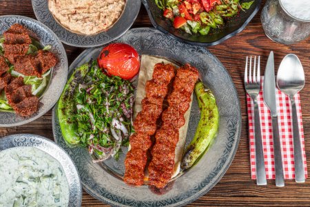 Gegrillter türkischer Adana Kebab mit gegrilltem Gemüse, Zwiebeln und Reis auf einem Holzbrett. Dunkler Hintergrund.