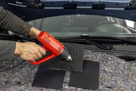 Auto service worker applies soundproof bitumen material to the hood of the car, adjusts the volume of the car or installs sound insulation. Car sound insulation installation process.