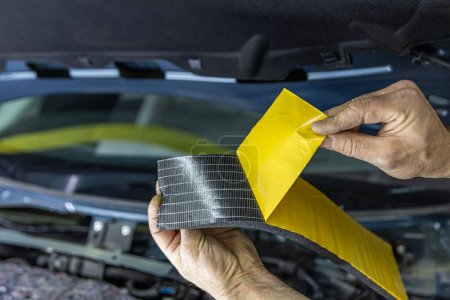 Auto service worker applies soundproof sponge material to the hood of the car, adjusts the sound of the car or installs sound insulation. Car sound insulation installation process.