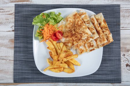 Turkish Cuisine Cheese Flatbread. Pita bread on wooden board with feta cheese, tomatoes, carrots and french fries. Traditional meal on wooden table. Turkish name ; Peynirli gozleme.