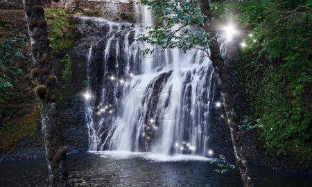 Téléchargez les photos : Cascade avec des étincelles de fées de lumière chatoyante dans une forêt magique - en image libre de droit