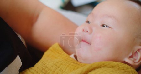 Fröhliches Baby in einem Senf-Lätzchen, das lächelt, während es in den Armen eines Elternteils liegt, mit einem Hintergrund, der den fröhlichen Ausdruck des Kindes unterstreicht