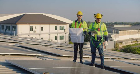 Photo for Technicians engineer in safety vests and helmets discussing analysis maintenance install solar panels on a metal roof, integrating sustainable energy solutions - Royalty Free Image