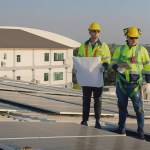 Technicians engineer in safety vests and helmets discussing analysis maintenance install solar panels on a metal roof, integrating sustainable energy solutions