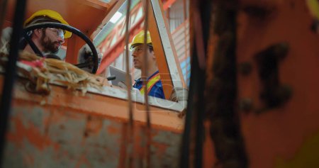 Construction workers in yellow hard hats and safety vests operate a construction lift machinery within an industrial environment, focus on occupational safety and teamwork