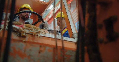 Téléchargez les photos : Les travailleurs de la construction portant des casquettes jaunes et des gilets de sécurité utilisent des ascenseurs de chantier dans un environnement industriel, en mettant l'accent sur la sécurité au travail et le travail d'équipe - en image libre de droit