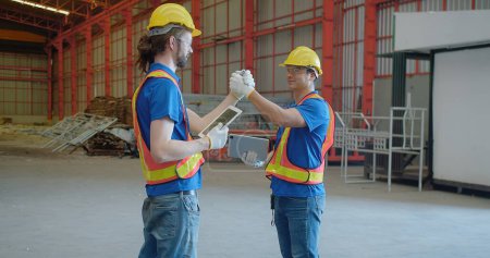 Photo for Two construction engineer workers in hard hats and vests engage in a friendly arm wrestling on a construction site, giving each other a fist bump blending teamwork with a light-hearted moment - Royalty Free Image