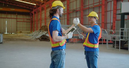 Dos trabajadores de ingeniería de construcción en sombreros y chalecos duros participan en una amistosa lucha de brazos en un sitio de construcción, dándose mutuamente un golpe de puño mezclando el trabajo en equipo con un momento alegre