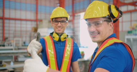 Zwei lächelnde Ingenieure Bauarbeiter in Schutzanzügen geben in einer industriellen Fertigungsfabrik die Daumen nach oben
