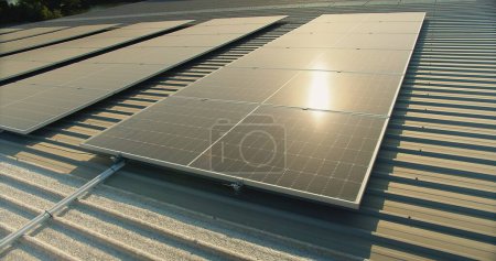 Sonnenkollektoren auf einem Wellblechdach, die Sonnenlicht reflektieren und alternative Energien präsentieren, Großaufnahme von Sonnenkollektoren auf dem Dach eines Industriegebäudes, die Sonnenlicht zur Energiegewinnung einfangen.