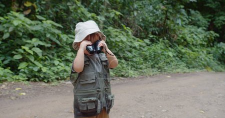 Foto de Un niño aventurero vestido con equipo explorador utiliza prismáticos en un exuberante bosque verde - Imagen libre de derechos
