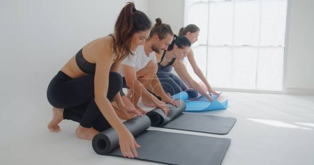 Téléchargez les photos : Groupe de jeunes gens de sport belle forme pliante tapis pour la session de cours de yoga au studio de sport - en image libre de droit