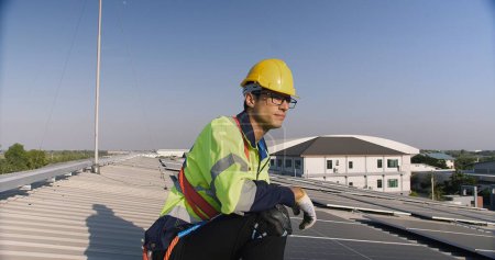Technician engineer worker in high visibility vest and safety helmet inspecting solar panels with laptop on a roof