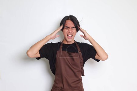 Téléchargez les photos : Portrait d'homme barista asiatique attrayant en tablier brun tenant la main sur le front, oublie quelque chose, et se regrette. Image isolée sur fond blanc - en image libre de droit