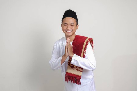 Téléchargez les photos : Portrait d'homme musulman asiatique attrayant en chemise blanche avec crâne montrant des excuses et geste de bienvenue. Image isolée sur fond gris - en image libre de droit