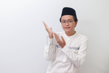Téléchargez les photos : Portrait de jeune homme musulman asiatique montrant le produit et pointant avec sa main et son doigt. Image isolée sur fond blanc - en image libre de droit