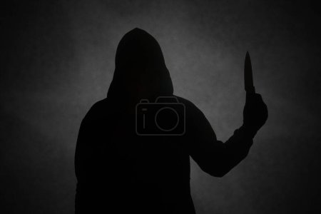 Téléchargez les photos : Homme mystérieux portant un sweat à capuche noir tenant un couteau pour poignarder quelqu'un. Crimes et concept de criminalité - en image libre de droit