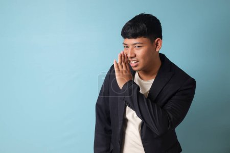 Téléchargez les photos : Portrait de jeune homme d'affaires asiatique en costume décontracté bavardant sur quelque chose. Image isolée sur fond bleu - en image libre de droit