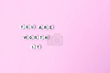 Foto de Vista superior de "usted vale la pena" citas hechas de cuentas sobre fondo pastel. concepto de motivación y éxito - Imagen libre de derechos
