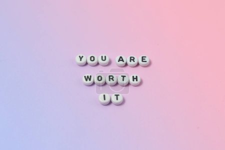 Foto de Vista superior de "usted vale la pena" citas hechas de cuentas sobre fondo pastel. concepto de motivación y éxito - Imagen libre de derechos