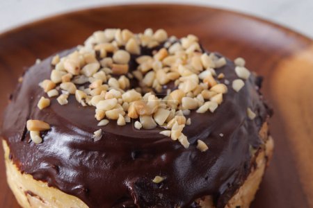 Téléchargez les photos : Gros plan détail photo de délicieux beignet glacé au chocolat sucré avec noix de cajou servi sur une assiette en bois. Image isolée sur fond blanc - en image libre de droit