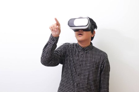 Téléchargez les photos : Portrait de l'homme asiatique en chemise à carreaux noire utilisant des lunettes de réalité virtuelle (VR) et essayant de toucher quelque chose devant lui. Image isolée sur fond blanc - en image libre de droit