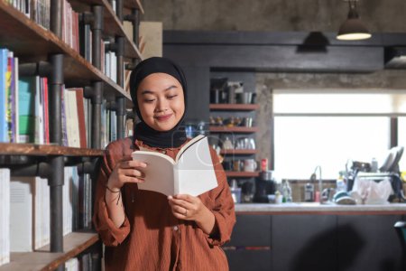 Photo for Portrait of Asian hijab woman holding book in front of library bookshelf. Muslim girl reading a book. Concept of literacy and knowledge - Royalty Free Image