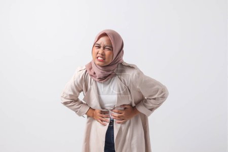 Téléchargez les photos : Portrait de femme hijab asiatique désagréable en costume décontracté souffrant de maux d'estomac. Concept de femme d'affaires. Image isolée sur fond blanc - en image libre de droit