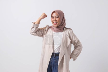 Téléchargez les photos : Portrait de femme hijab asiatique excitée en costume décontracté levant son poing, célébrant le succès. Concept de femme d'affaires. Image isolée sur fond blanc - en image libre de droit