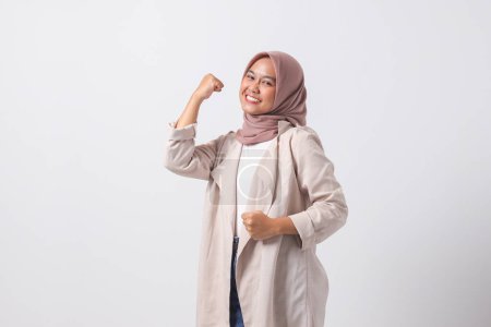 Téléchargez les photos : Portrait de femme hijab asiatique excitée en costume décontracté levant son poing, célébrant le succès. Concept de femme d'affaires. Image isolée sur fond blanc - en image libre de droit