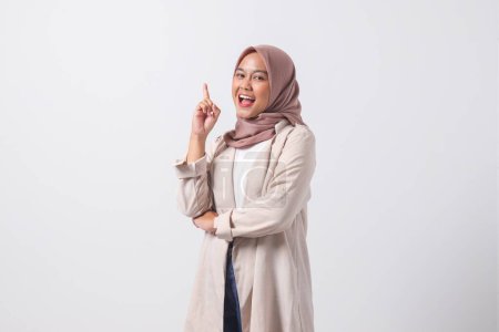 Téléchargez les photos : Portrait de femme asiatique excitée hijab en costume décontracté pointant son index et rappelant quelque chose à faire. Concept de femme d'affaires. Image isolée sur fond blanc - en image libre de droit