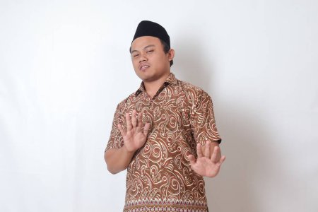 Photo for Portrait of unpleasant Asian man wearing batik shirt and songkok forming a hand gesture to avoid something. Advertising concept. Isolated image on gray background - Royalty Free Image