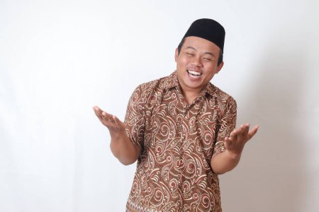 Photo for Portrait of excited Asian man wearing batik shirt and songkok spreading his hands sideways. Welcoming and greeting someone. Isolated image on gray background - Royalty Free Image