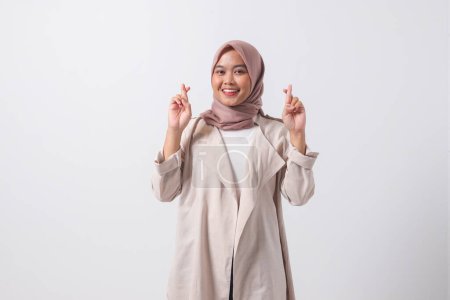 Téléchargez les photos : Portrait d'une jolie femme hijab asiatique en costume décontracté faisant signe à la main, un geste symbolique avec les doigts croisés montrant bonne chance. Image isolée sur fond blanc - en image libre de droit