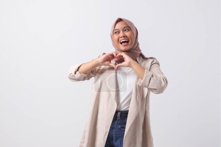 Téléchargez les photos : Portrait de femme hijab asiatique attrayante en costume décontracté parle de ses propres sentiments, fait un geste de cœur sur la poitrine, exprime de la sympathie et de l'amour, sourit positivement. Image isolée sur fond blanc - en image libre de droit