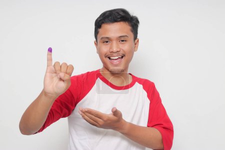 Foto de Retrato del emocionado hombre asiático mostrando el dedo meñique sumergido en tinta púrpura después de la votación para las elecciones generales o Pemilu para el presidente y el gobierno de Indonesia. Aislado sobre fondo blanco - Imagen libre de derechos