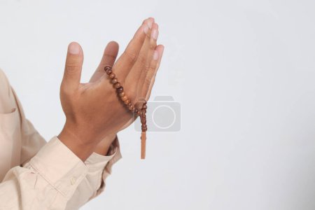 Close up hand of religious Asian muslim man in koko shirt with skullcap praying earnestly with his hands raised, holding islamic beads. Devout faith concept. Isolated image on white background